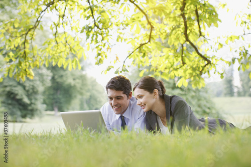 Photo: Business people laying in grass using laptop Business people laying in grass using laptop
