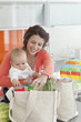 Woman holding baby and unloading groceries from reusable bag