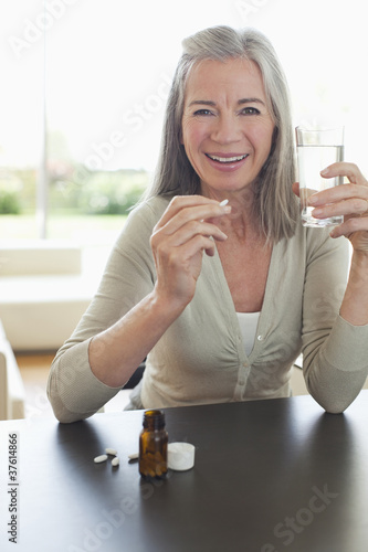 Foto: Smiling woman holding glass of water and taking pills Smiling woman holding glass of water and taking pills