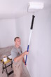 Decorator using a roller extension to paint a ceiling white
