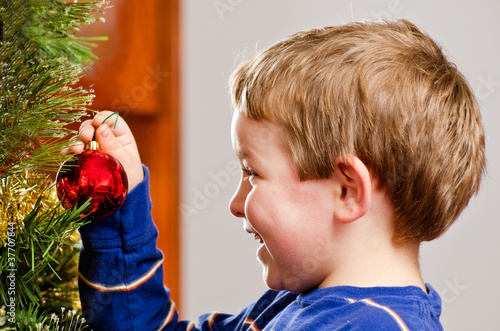 Photo: Young boy decorates Christmas Tree for holiday. Young boy decorates Christmas Tree for holiday.