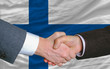 businessmen handshake after good deal in front of finland flag