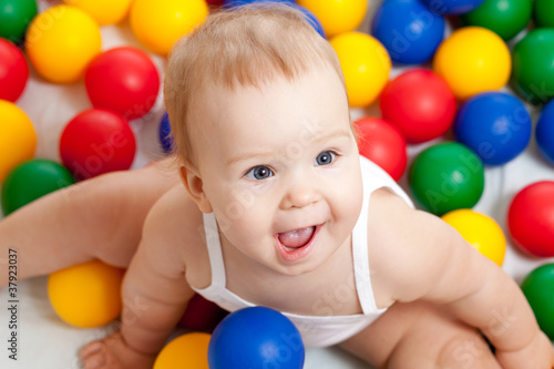 Photo: Portrait of a adorable infant sitting among colorful balls Portrait of a adorable infant sitting among colorful balls