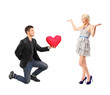 A romantic man on his knees holding a red heart shaped pillow an