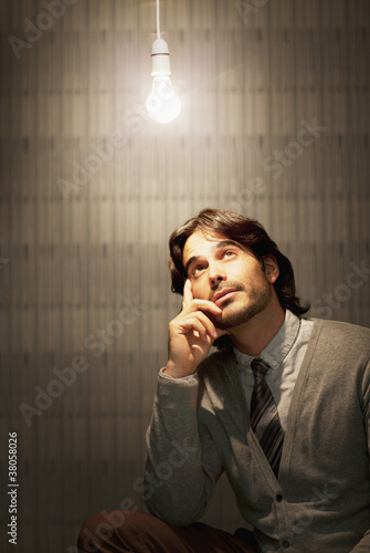 Photo: Pensive businessman sitting under illuminated light bulb Pensive businessman sitting under illuminated light bulb