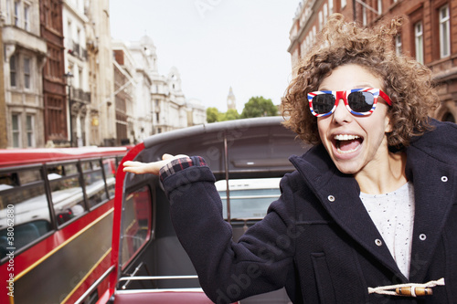 Photo: Portrait of exuberant woman wearing British flag sunglasses and riding double decker bus in London Portrait of exuberant woman wearing British flag sunglasses and riding double decker bus in London