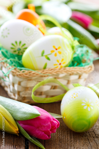 Photo: easter basket,eggs and tulips on wooden board easter basket,eggs and tulips on wooden board