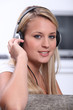 A blond woman looking at us with headphones on her head.