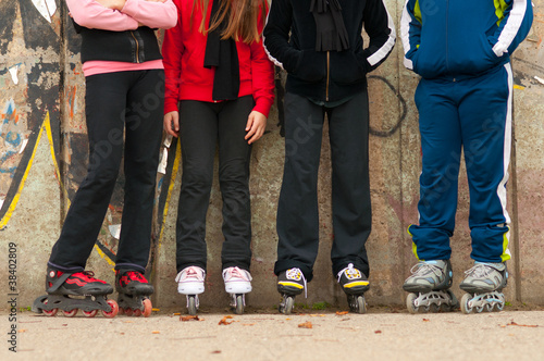 Photo: Group of teenagers in roller skates standing beside the wall Group of teenagers in roller skates standing beside the wall