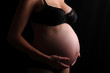 Pregnant woman touching her belly with hands, dark barkground