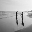 small boy plays by the ocean as his dad watches on