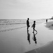 small boy plays by the ocean as his dad watches on