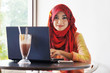 Stylish muslim woman wearing red scarf smiling while typing on h