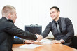 Photo: Young business man shaking hands with colleague across the table Young business man shaking hands with colleague across the table