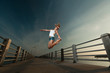Young woman jumping in sunset light on a pier