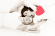 Young couple holding red heart together lying in a bed Young couple holding red heart together lying in a bed