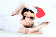 Couple holding red heart together lying in a bed and kissing Couple holding red heart together lying in a bed and kissing