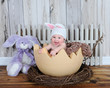 adorable baby in bunny hat sitting in giant easter egg