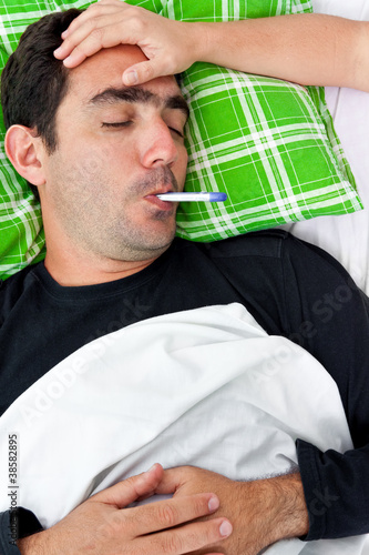 Photo: Sick hispanic man laying in bed with a thermometer Sick hispanic man laying in bed with a thermometer