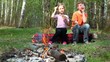 Boy and little girl sit, they drink juice and watch at bonfire