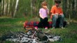 Boy and girl sit on log, they drink juice and watch at bonfire