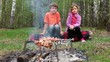 Boy and girl sit on log and watch at fresh meat on embers