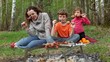 Mom and kids sit on grass cover by plaid and eats kebab