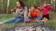 Mom and kids sit on grass cover by plaid and eats kebab Mom and kids sit on grass cover by plaid and eats kebab
