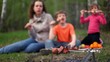 Mom and two kids, sit on grass cover by plaid and eats kebab