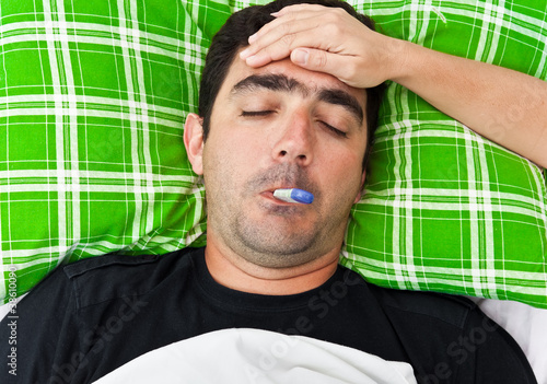Photo: Sick hispanic man laying in bed with fever Sick hispanic man laying in bed with fever