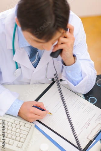 Photo: Medical doctor speaking phone and notes in clipboard. Top view Medical doctor speaking phone and notes in clipboard. Top view