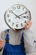 Mann haelt eine Uhr vor seinem Gesicht als Symbol für Zeitarbeit