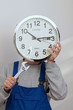 Mann haelt eine Uhr vor seinem Gesicht als Symbol für Zeitarbeit