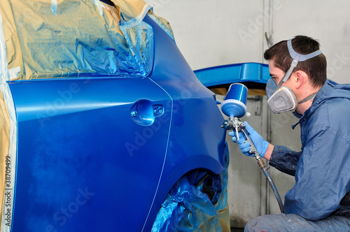 Photo: Worker painting a blue car. Worker painting a blue car.