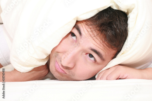 Photo: Man trying to sleep with a pillow over his head and close to wak Man trying to sleep with a pillow over his head and close to wak
