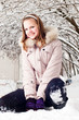 Beautiful young girl sits on to snow in warm clothes in winter o