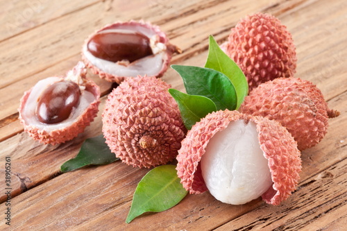 Photo: Lychee with leaves on a wooden table. Lychee with leaves on a wooden table.