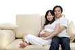 Asian couple. Husband and 8 months pregnant wife sitting on sofa