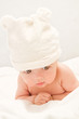 Cute baby lying on the blanket and is wearing a white hat.