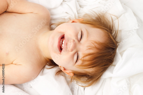 Photo: Happy child laughing and laying in white sheets Happy child laughing and laying in white sheets