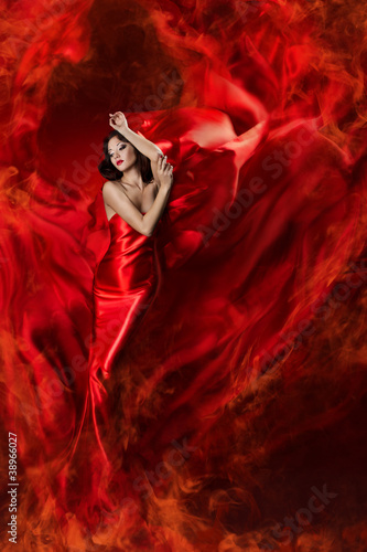 Foto: Beautiful woman in red waving silk dress as a fire flame. Lookin Beautiful woman in red waving silk dress as a fire flame. Lookin