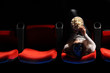 a pretty young woman sitting in a row of red chairs in a theater