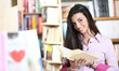 smiling female student with book in hands in a bookstore - model