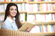 smiling female student with book in hands sitting in a chair in
