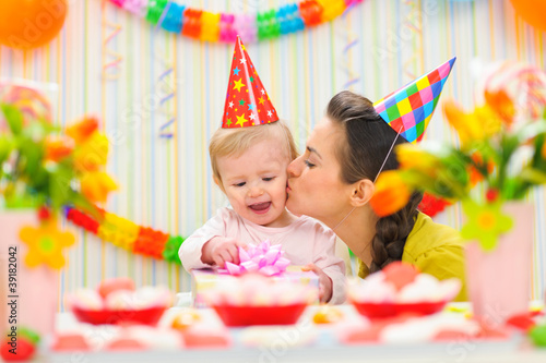 Photo: Mother kissing her happy while baby checking present Mother kissing her happy while baby checking present