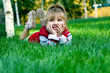 The small beautiful girl sits on a green lawn and laughs