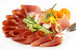 Slices of prosciutto rolled up and arranged with cucumber and pa