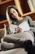 Portrait of a happy young woman lying on couch with book