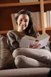 Portrait of a happy young woman lying on couch with book