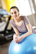 Attractive young woman leaning on an exercise ball at the gym